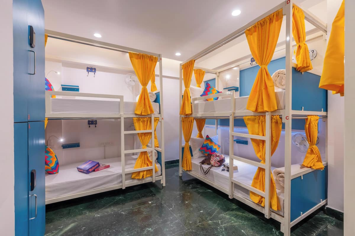 A room with bunk beds, each with yellow curtains tied at the top, white bedding, and a blue cabinet.