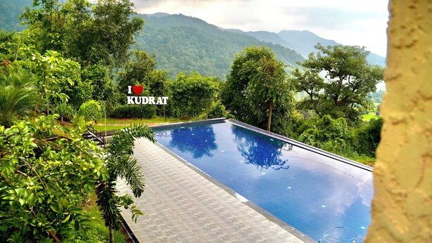A swimming pool surrounded by lush greenery and mountains in the background. - Kudrat Resort : Jim Corbett (Chauk Patelia)