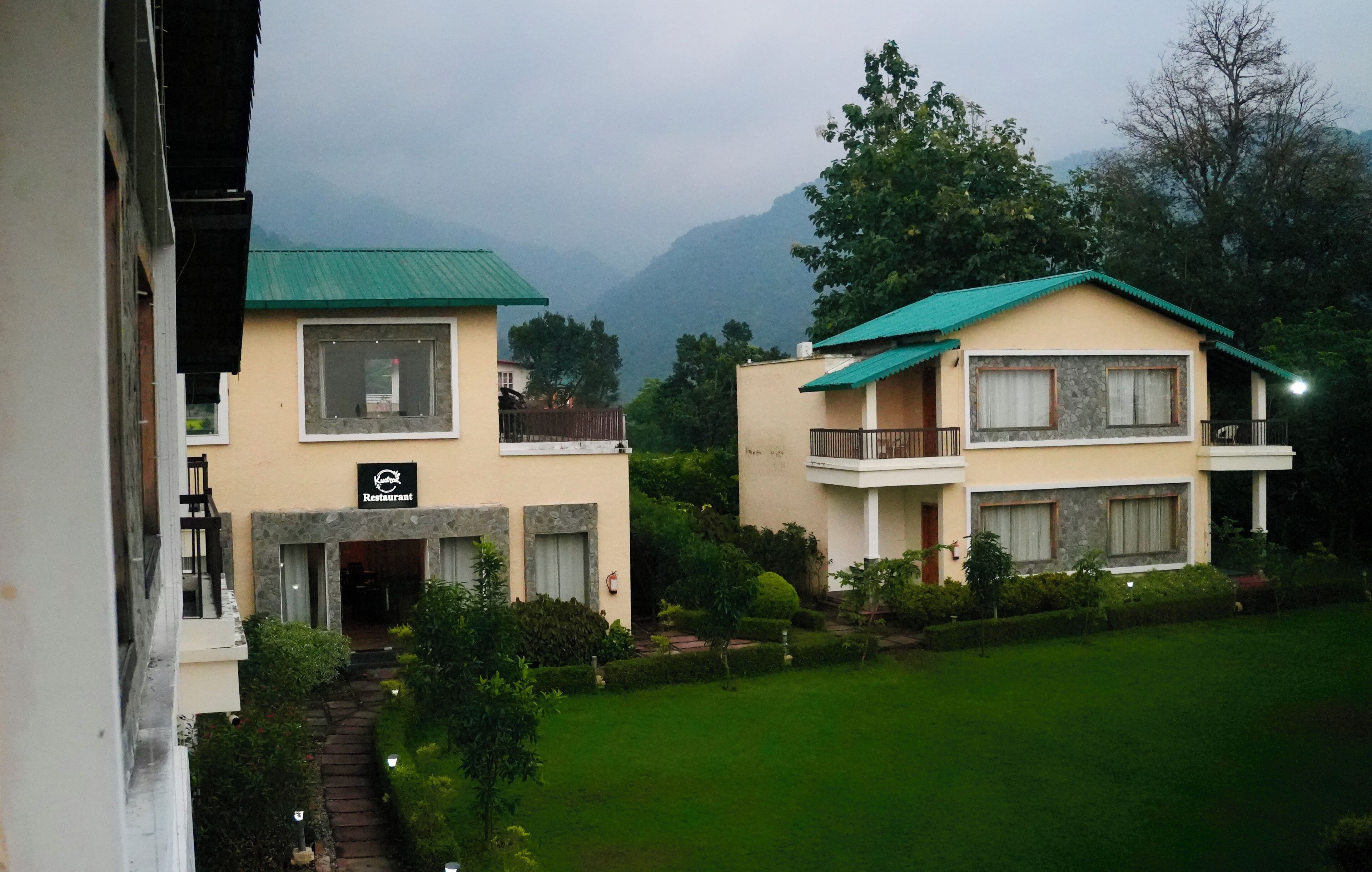 A two-story building with a restaurant sign, surrounded by greenery and mountains in the background.