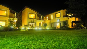 A multi-story building with illuminated windows and a well-maintained lawn in front. - Kudrat Resort : Jim Corbett (Chauk Patelia)