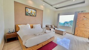 A bedroom with a bed, a wooden nightstand, a chair, a glass coffee table, a red rug, a wooden wardrobe, and a window with a view. - Kudrat Resort : Jim Corbett (Chauk Patelia)