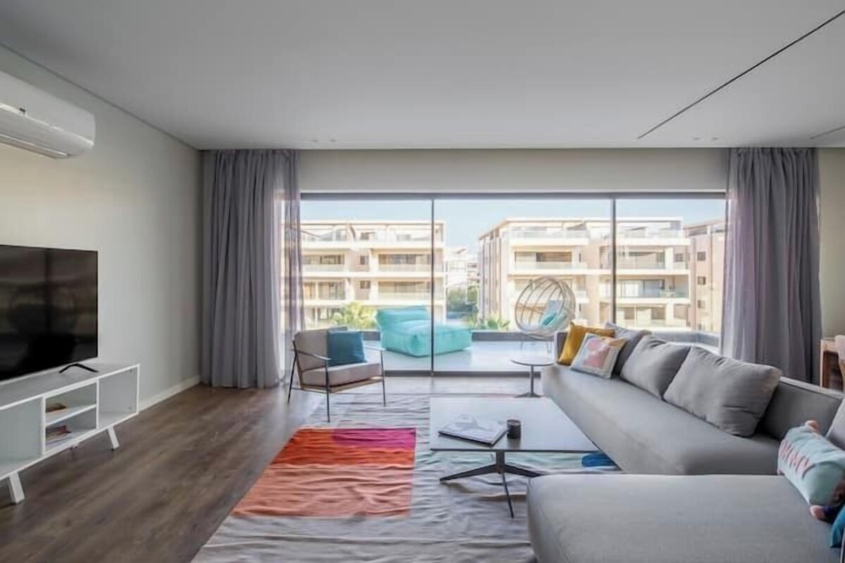 A modern living room with a large flat-screen TV, grey sofa, and a colorful rug.