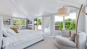 A bedroom with a bed, a sofa, a floor lamp, and large windows.