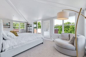 A bedroom with a bed, a sofa, a floor lamp, and large windows.