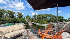 Une terrasse en bois avec un canapé, deux chaises en bois, une petite table ronde et un hamac.