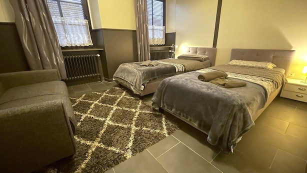 A bedroom with two beds, a sofa, a radiator, and a window with curtains.
