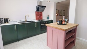 Une cuisine moderne avec des meubles de couleur vert foncé, un îlot central rose et une lucarne.