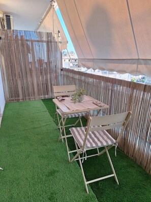 A tented outdoor area with artificial grass, a table, chairs, and a bamboo fence.