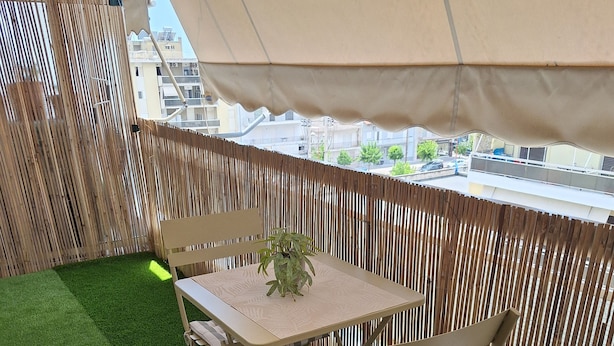 Un balcón con mesa y sillas, una planta en maceta y vistas a edificios.