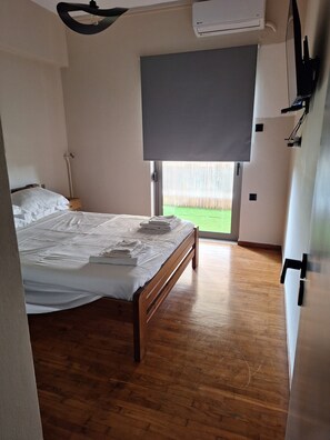 A bedroom with a wooden bed, a window with a view of a grassy area, and an air conditioning unit on the wall. - Faron 203 Apartment (Kalamata)