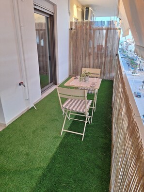 A balcony with artificial grass, a table with chairs, a potted plant, and a view of the street.