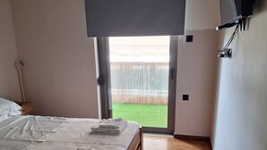 Un dormitorio con cama, piso de madera y vista a un césped verde a través de un ventanal.