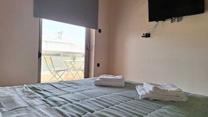 Una habitación de hotel con una cama, un televisor en la pared y un balcón con sillas y una mesa.
