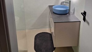 Un baño moderno con ducha de vidrio, un lavabo azul y un espejo redondo.