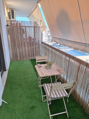 Ein Balkon mit künstlichem Gras, einem Tisch, Stühlen und einem Blumentopf.