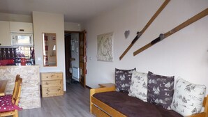Une pièce chaleureuse avec un lit en bois, une chaise en bois, une petite commode en bois et un coin cuisine équipé d’un four à micro-ondes.