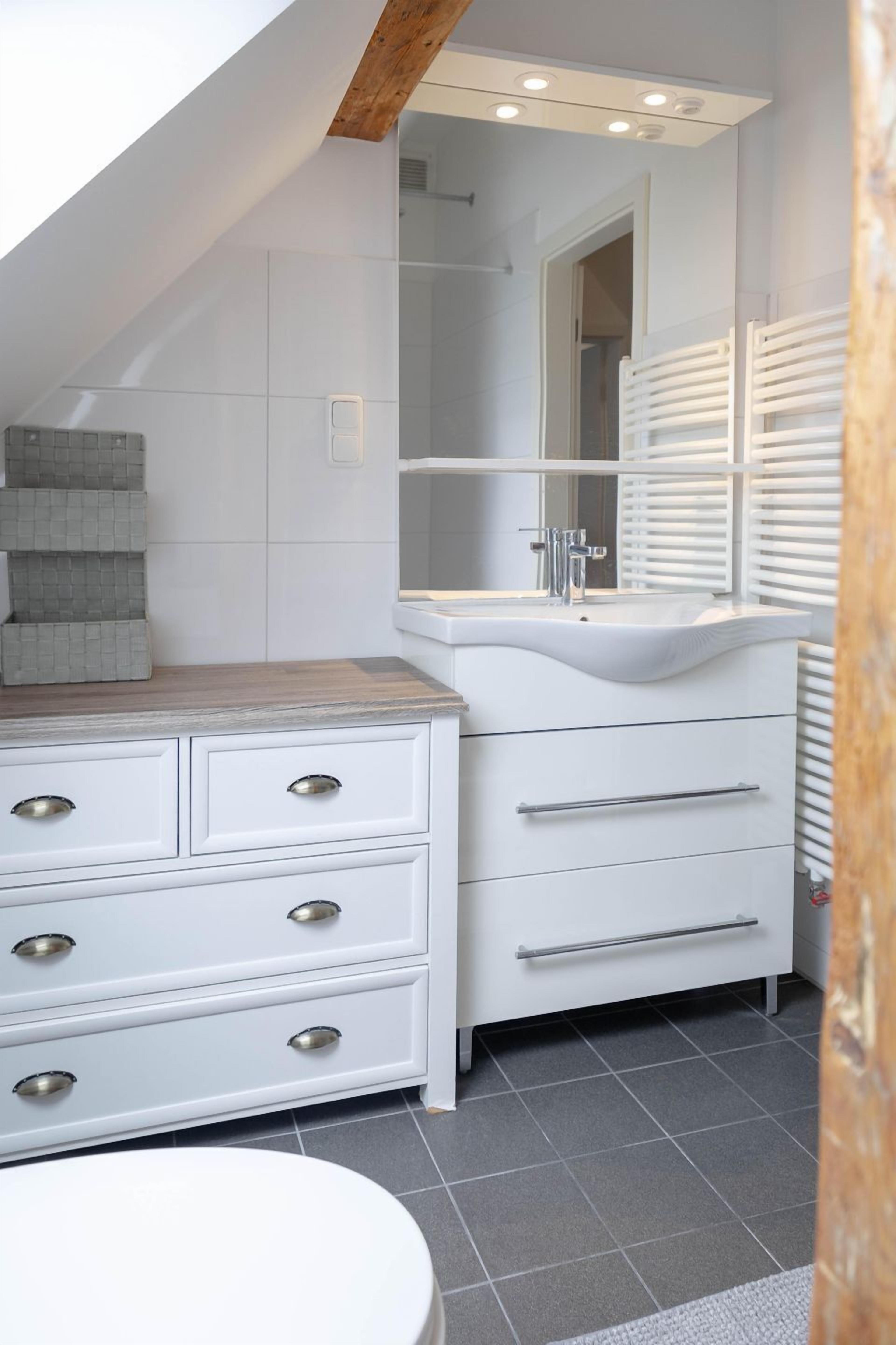 Un baño moderno con un tocador blanco, un espejo grande y piso de baldosas.