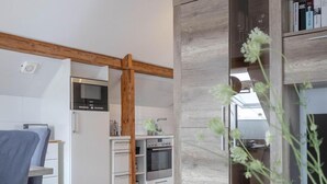 A modern kitchen with wooden beams, white cabinetry, and a dining area with a table set for two. - Ahoy Amore (Sylt)