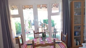 A dining area with a table set for four, surrounded by chairs, and a view of the outdoors through large windows. - Corse, San giuliano, 50 kms de Bastia, maison à 2mn de la mer, animaux acceptés (san giuliano)