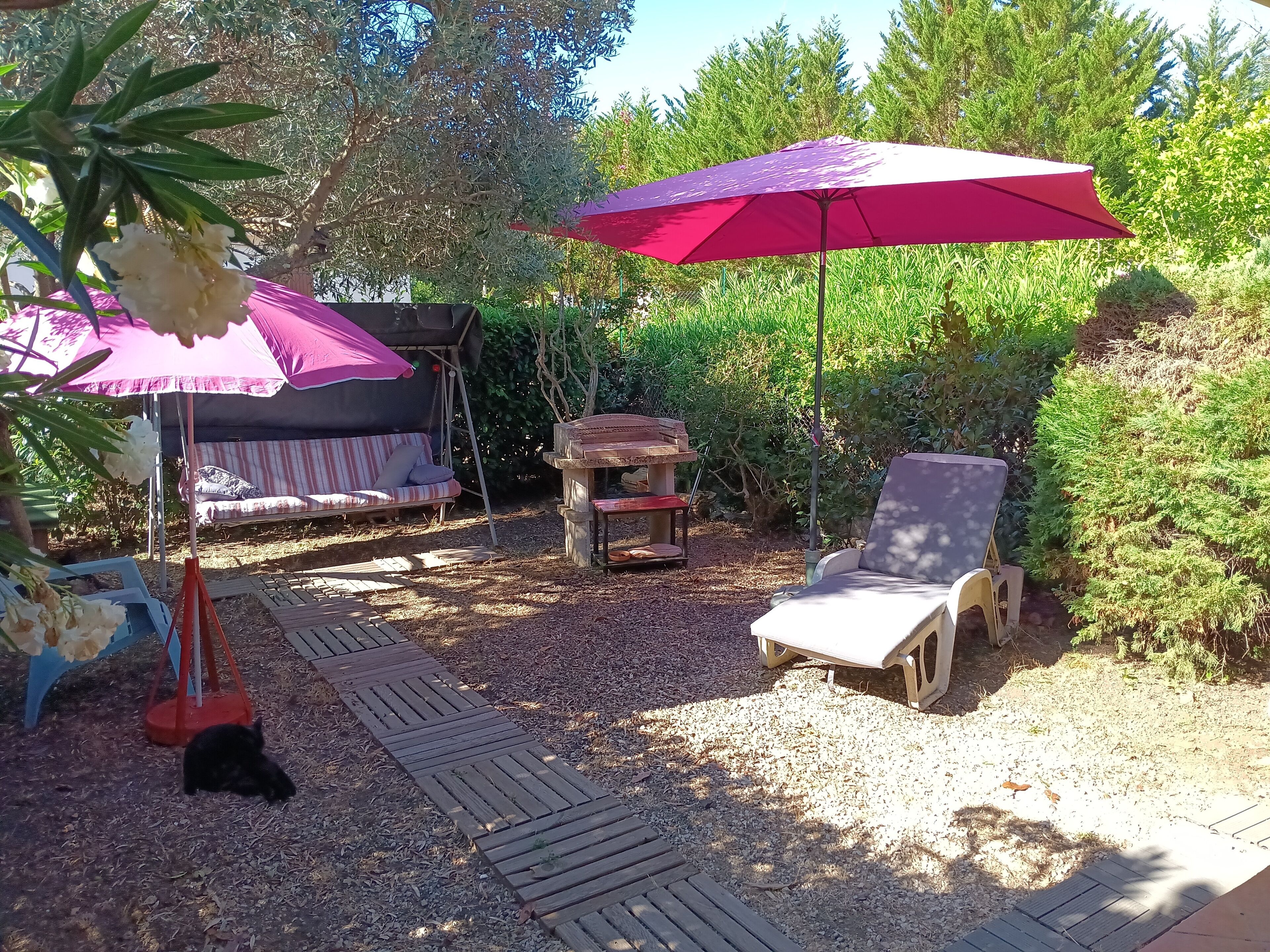 A garden patio with a wooden deck, a striped sofa, a wooden table, and a red umbrella.
