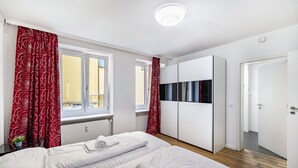 A hotel room with two beds, a wardrobe, and a window with curtains. - Aldars Urban Trio Suites No.12 with Wi-Fi and Air Conditioning (München)
