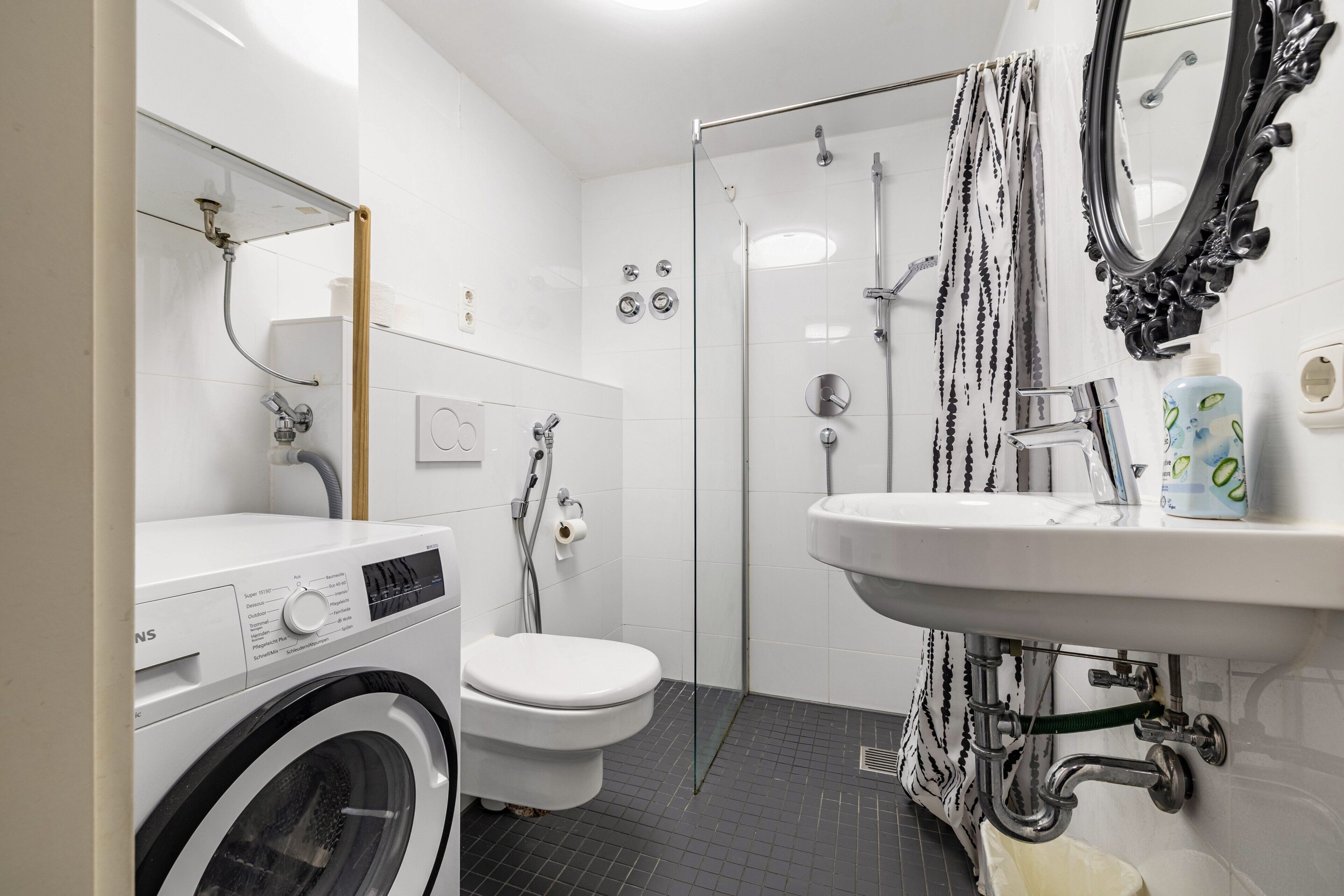 Ein modernes Badezimmer mit Waschmaschine, Toilette, Dusche und Waschbecken.
