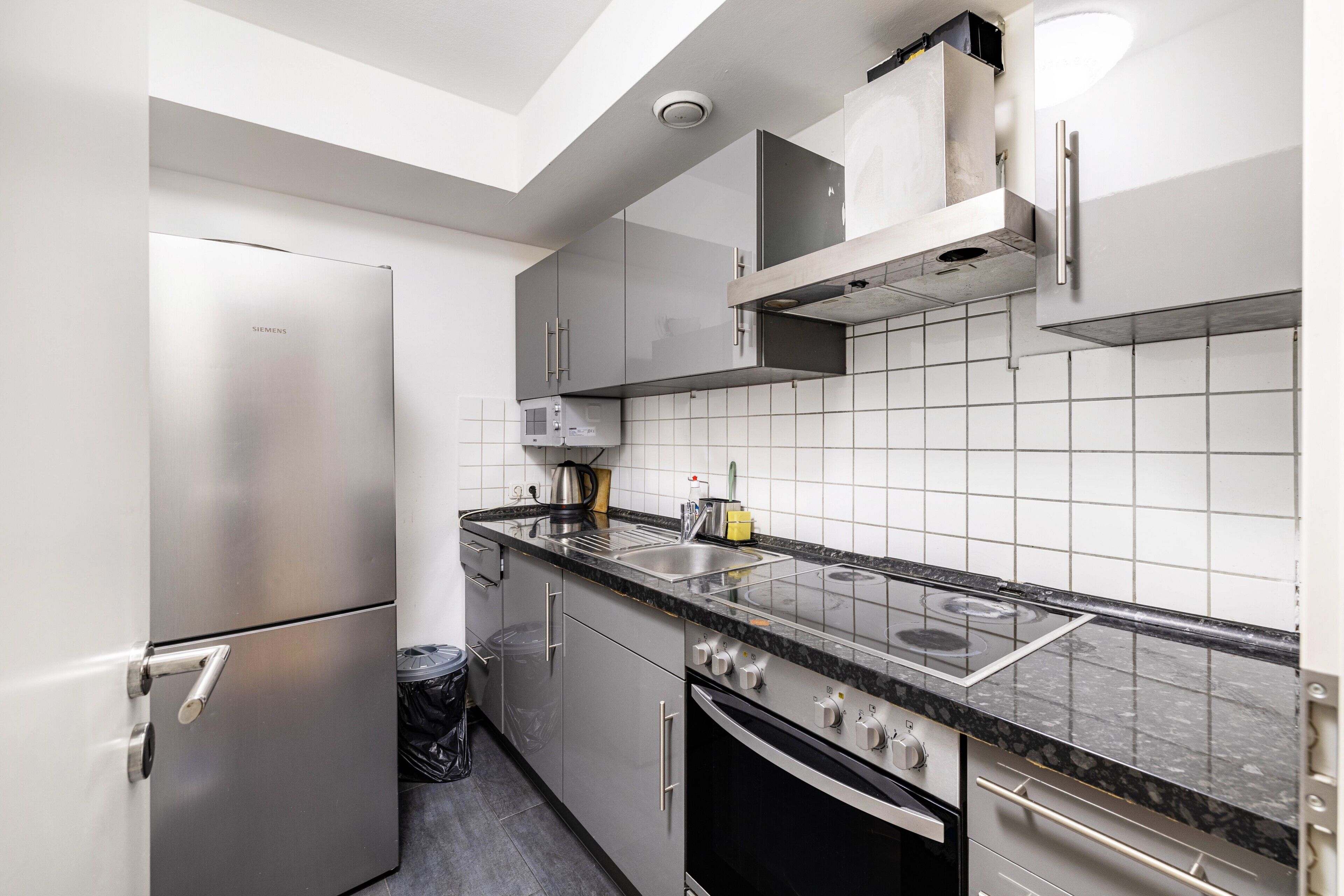 Una cocina moderna con electrodomésticos de acero inoxidable, encimera negra y salpicadero de azulejos blancos.