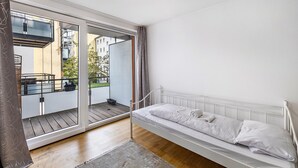 A bedroom with a bed, a sliding glass door to a balcony, and a view of buildings outside. - Aldars Urban Trio Suites No.12 with Wi-Fi and Air Conditioning (München)