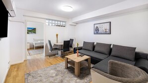 A modern living room with a sofa, a coffee table, and a dining area with chairs and a table. - Aldars Urban Trio Suites No.12 with Wi-Fi and Air Conditioning (München)