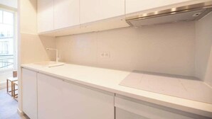 Une cuisine moderne avec des armoires blanches, une hotte de cuisinière en acier inoxydable et une fenêtre qui laisse entrer la lumière naturelle.