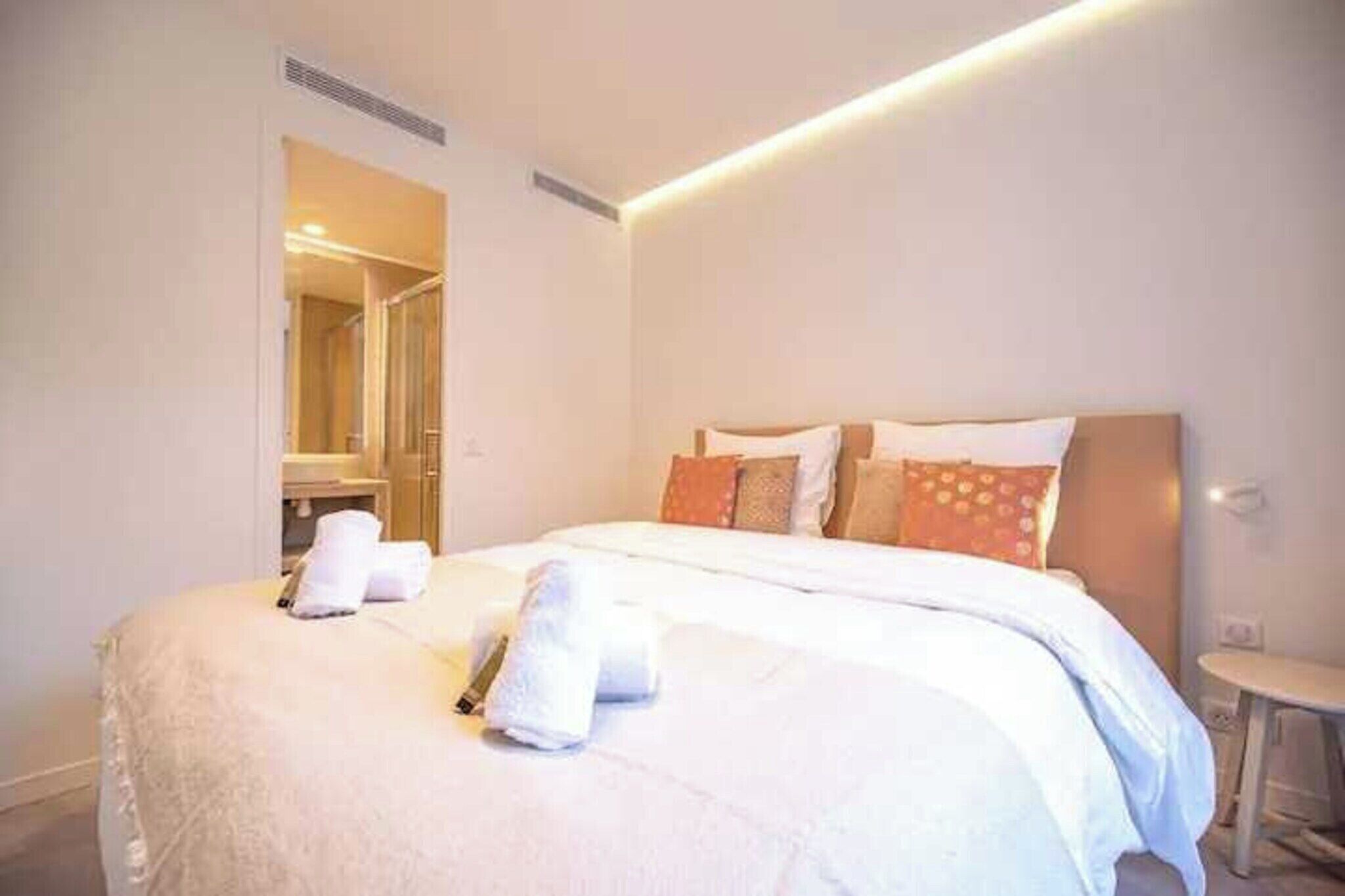 Une chambre d’hôtel moderne, avec un lit soigneusement fait, une petite table et une salle de bain visible à travers une porte ouverte.