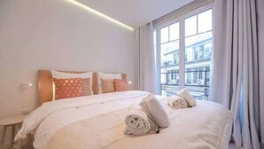 Une chambre d’hôtel avec un grand lit, une petite table de chevet et une vue sur les immeubles par la fenêtre.