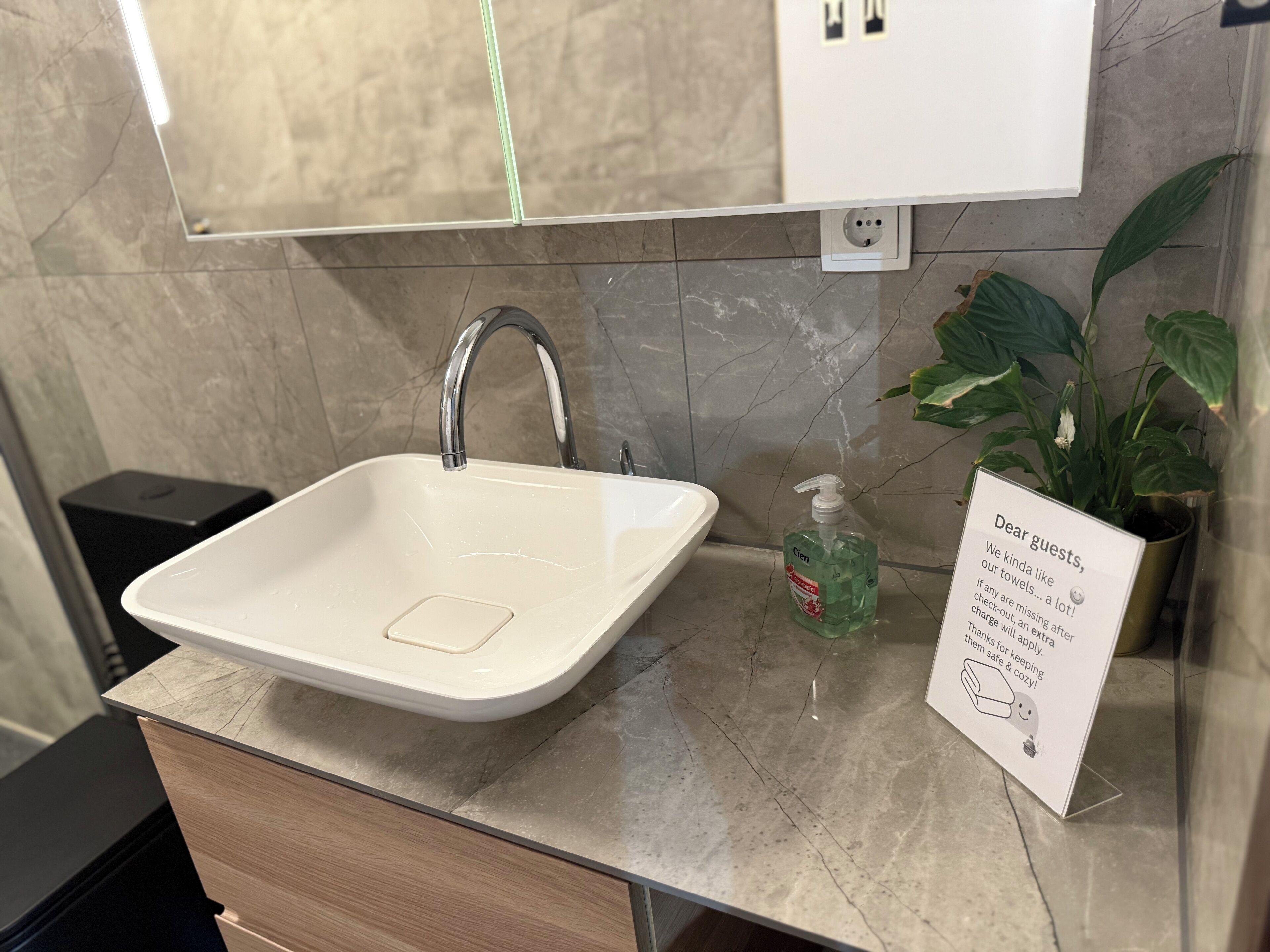 Ein Waschbecken mit Spiegel darüber, einer Seifenspender und ein Schild mit einer Botschaft für Gäste.