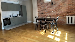 A modern kitchen with grey cabinets, a black oven, and a dining area with a wooden table and chairs. - Browar Hevelius Comfort Apartments by GA (Gdańsk)