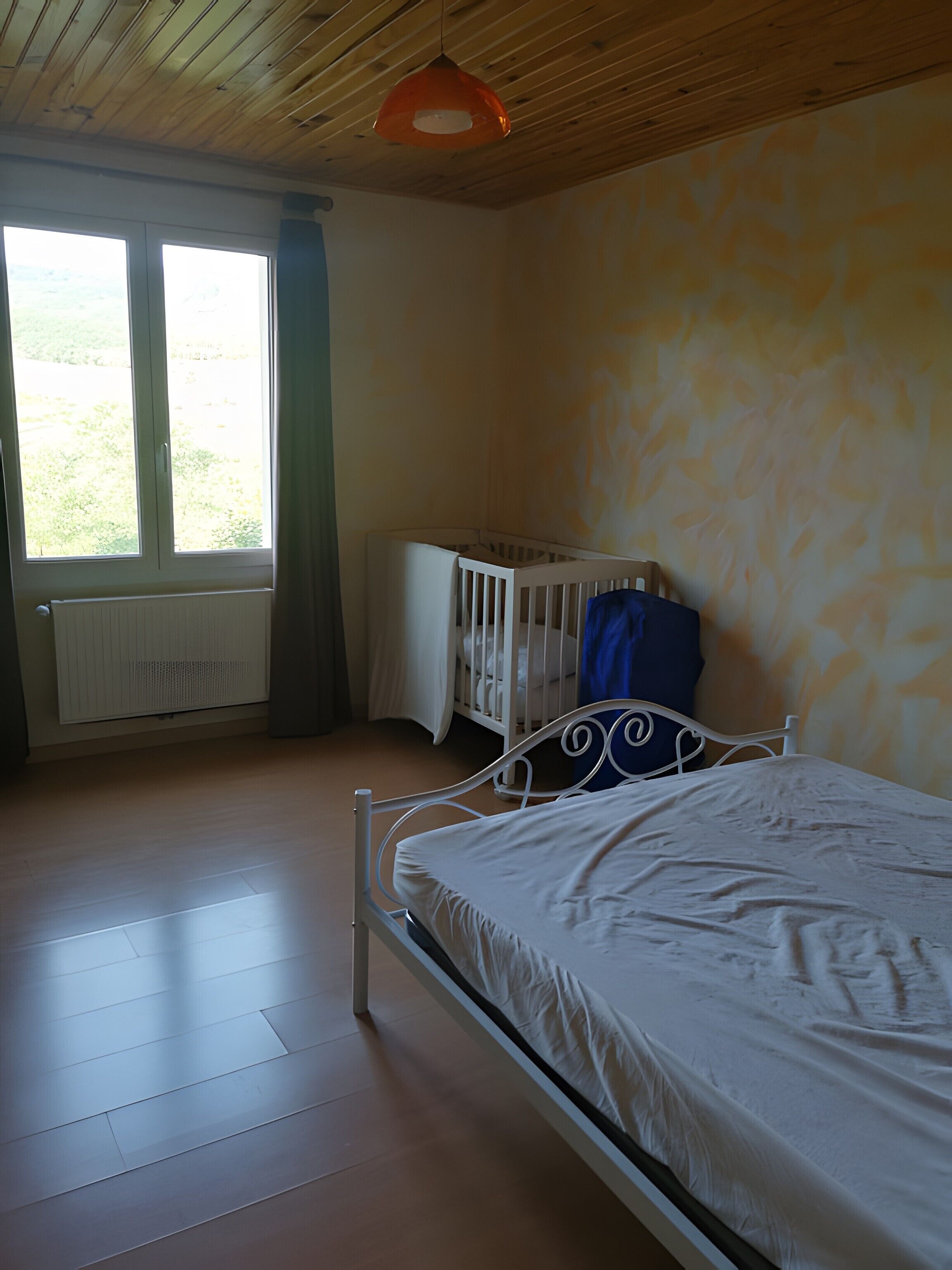 Quarto com cama, berço, radiador e janela.