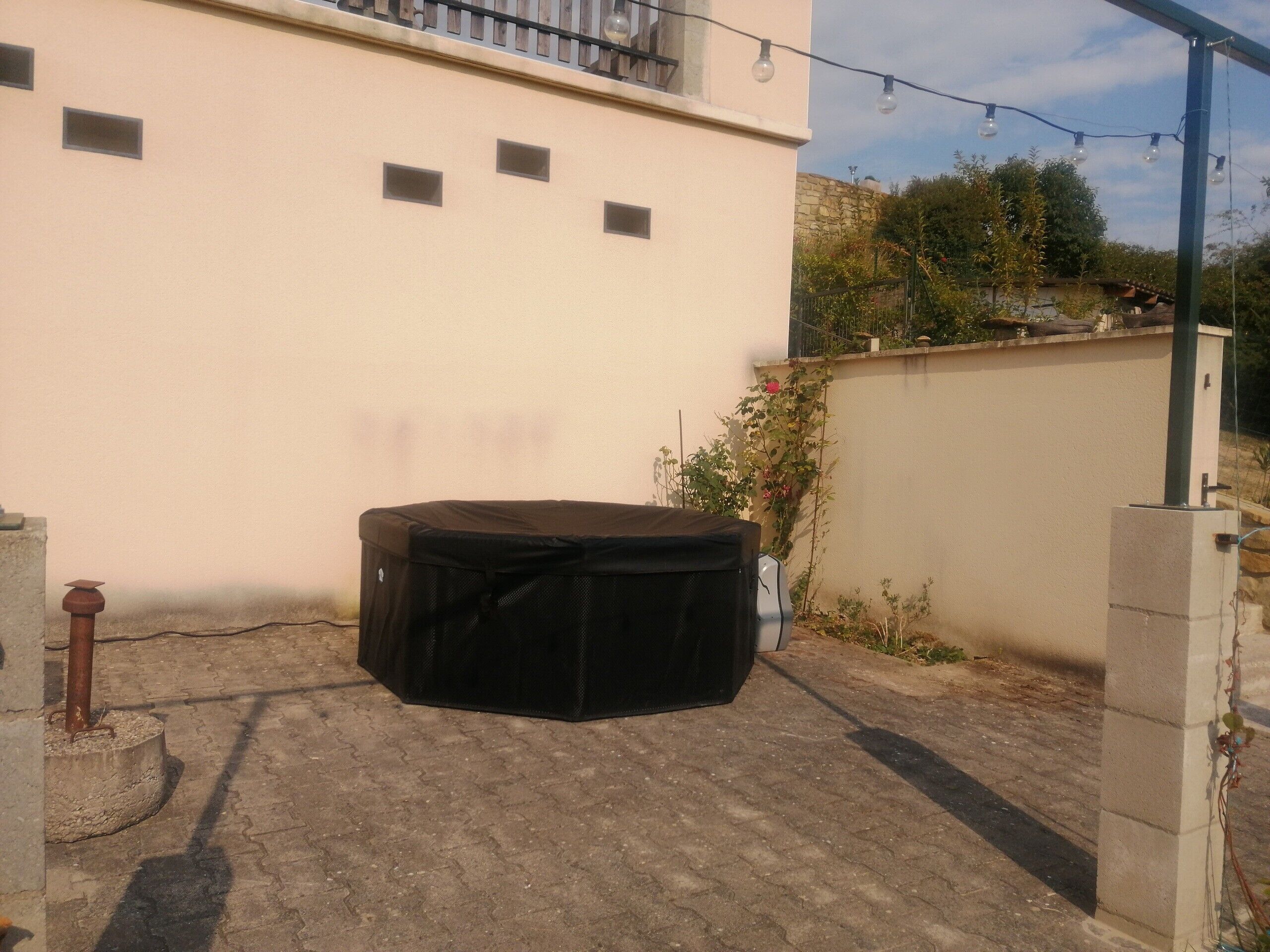 Un espacio exterior techado con un jacuzzi, una pared con ventanas pequeñas y una guirnalda de luces.