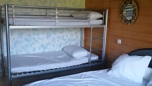 Ein Stockbett mit zwei Liegeebenen, einem Einzelbett und einem Spiegel an der Wand.
