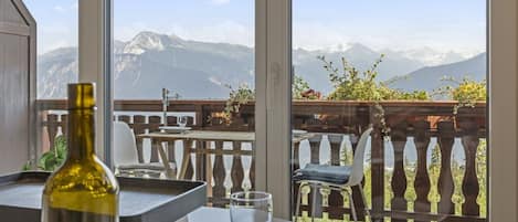 A balcony with a mountain view, a table with a bottle and glass, and a chair.