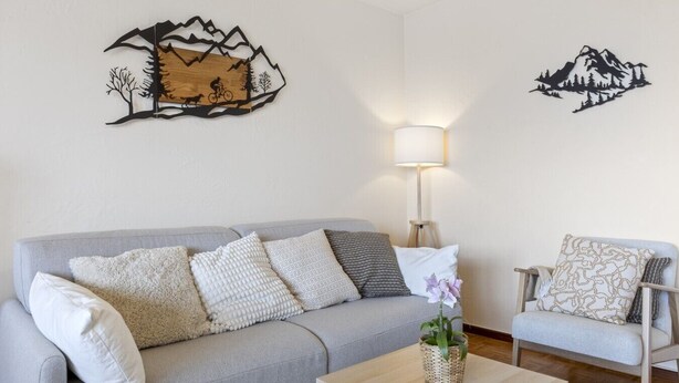 Ein Wohnzimmer mit grauem Sofa, einem Holztisch und einer Lampe.