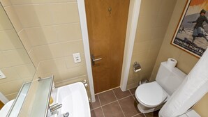 Ein Badezimmer mit Holztür, einer weißen Toilette, einem weißen Waschbecken inklusive Spiegel und einem Poster an der Wand.