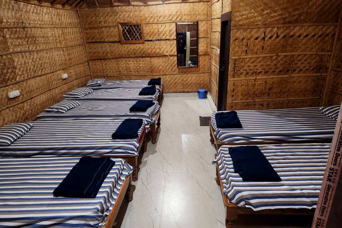 A room with four wooden beds, each with striped bedding and dark pillows. The room has a tiled floor and a small window with a grid pattern.