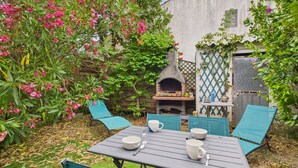 An outdoor patio with a table set for dining, surrounded by green chairs, and a pizza oven in the background.