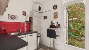 A compact kitchen with a red backsplash, a coffee shop sign, a clock, and a view of a garden through a door.