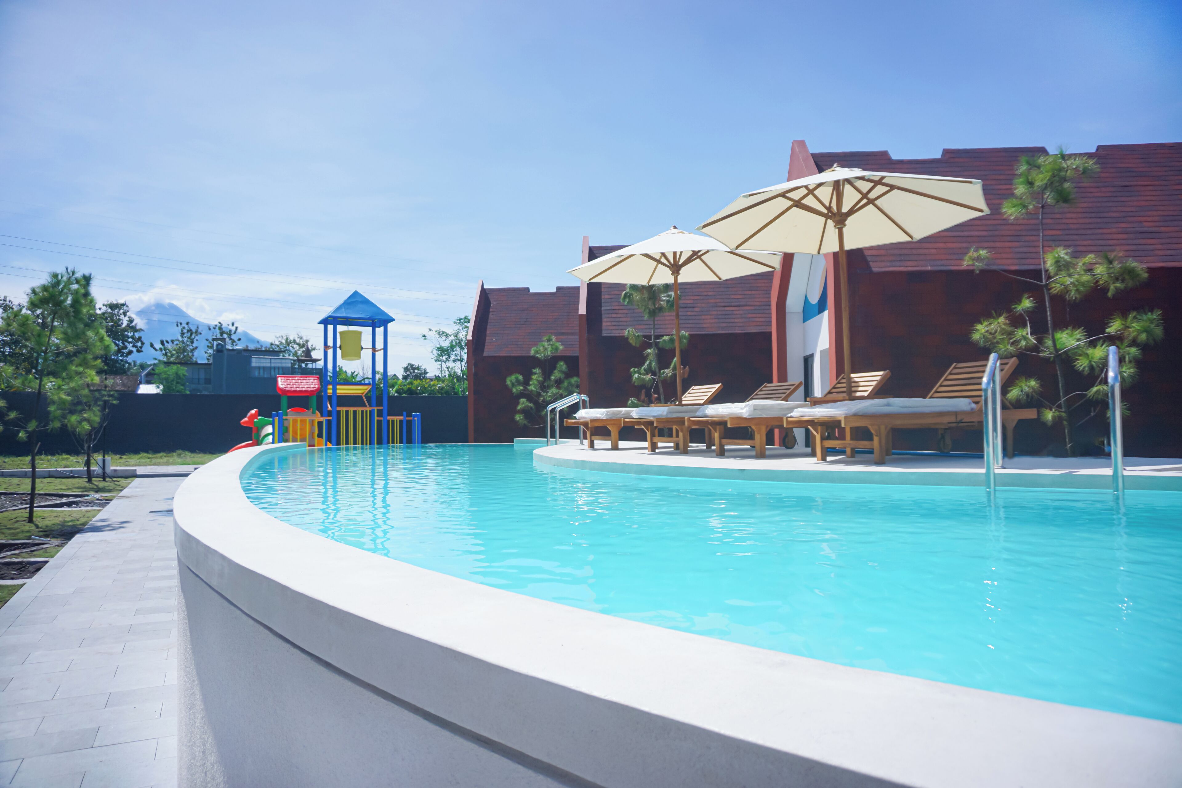 A swimming pool with lounge chairs and umbrellas, surrounded by buildings and trees.