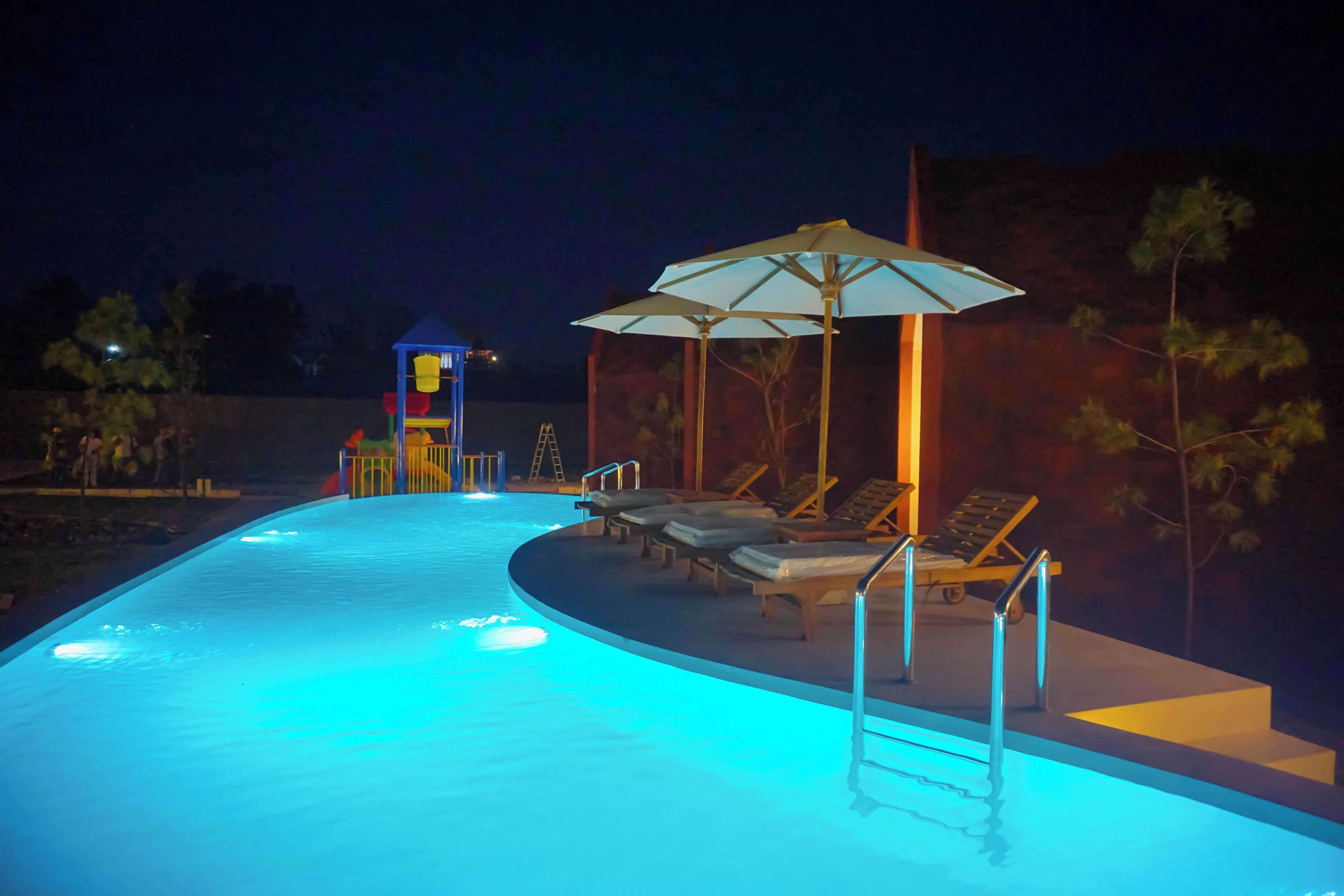 A swimming pool with a blue-lit edge, lounge chairs, and umbrellas.