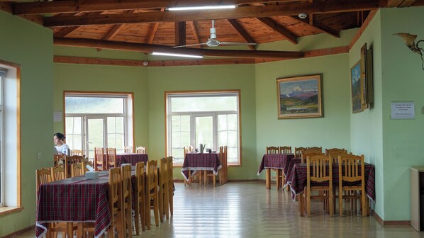 A dining area with wooden tables and chairs, large windows, and a ceiling fan. - Bayankhad Star Lodge (Ulaanbaatar)