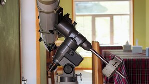 A telescope mounted on a tripod in a room with wooden floors and a window. - Bayankhad Star Lodge (Ulaanbaatar)