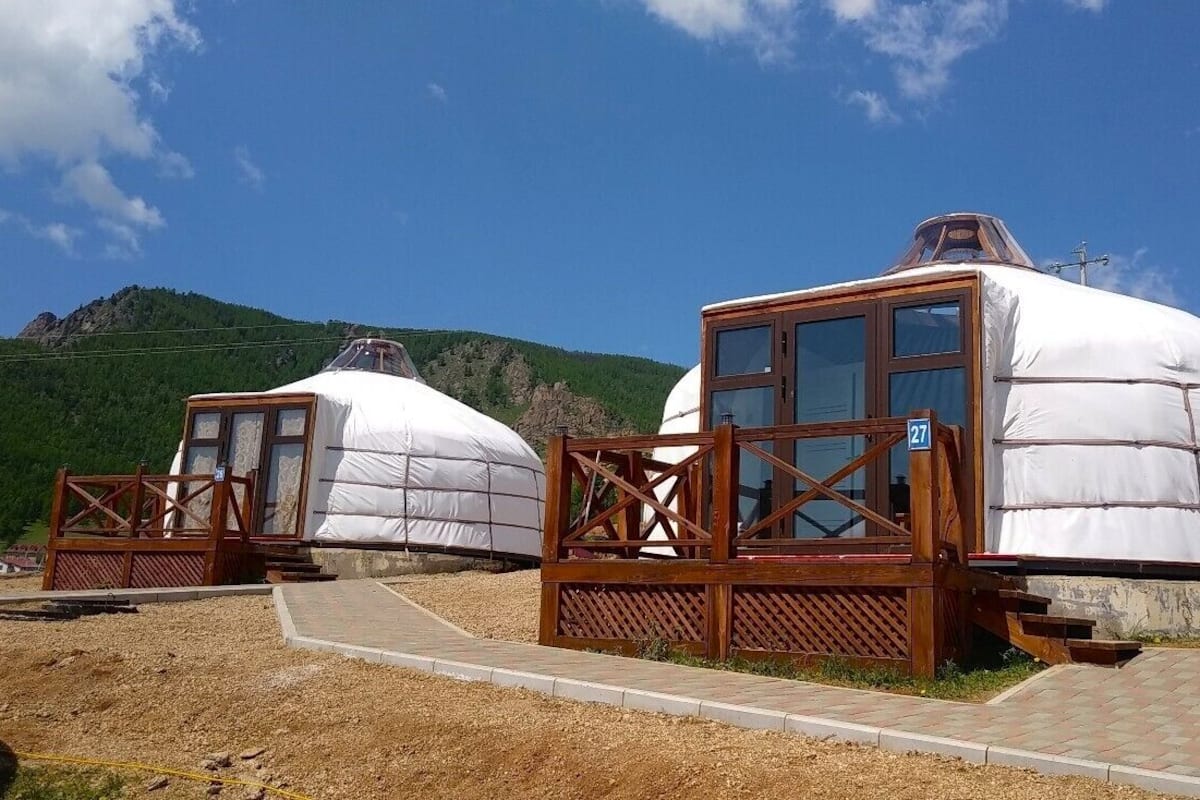 Two yurts with wooden walkways and a mountain backdrop.