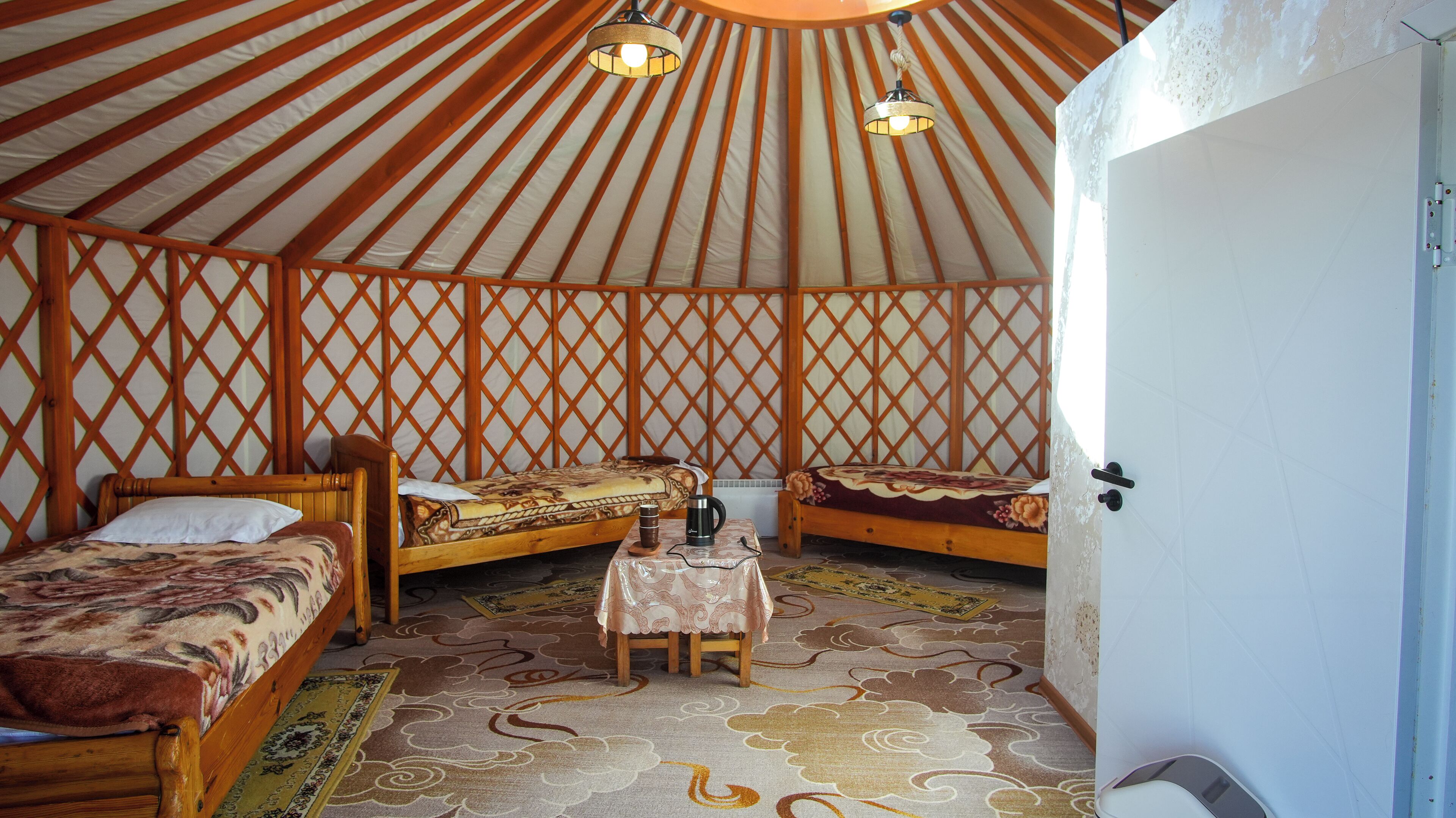 A yurt with three wooden beds, a small table with a kettle, and a patterned rug.