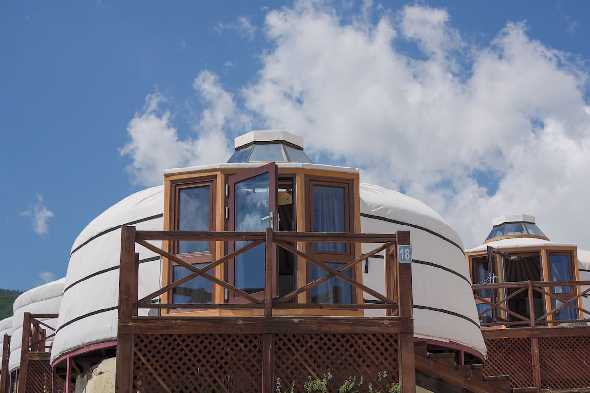 Yurts with wooden frames and windows, set against a clear sky.